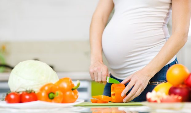 Pregnant Woman Slicing Vegetables as Part of Healthy Pregnancy Diet